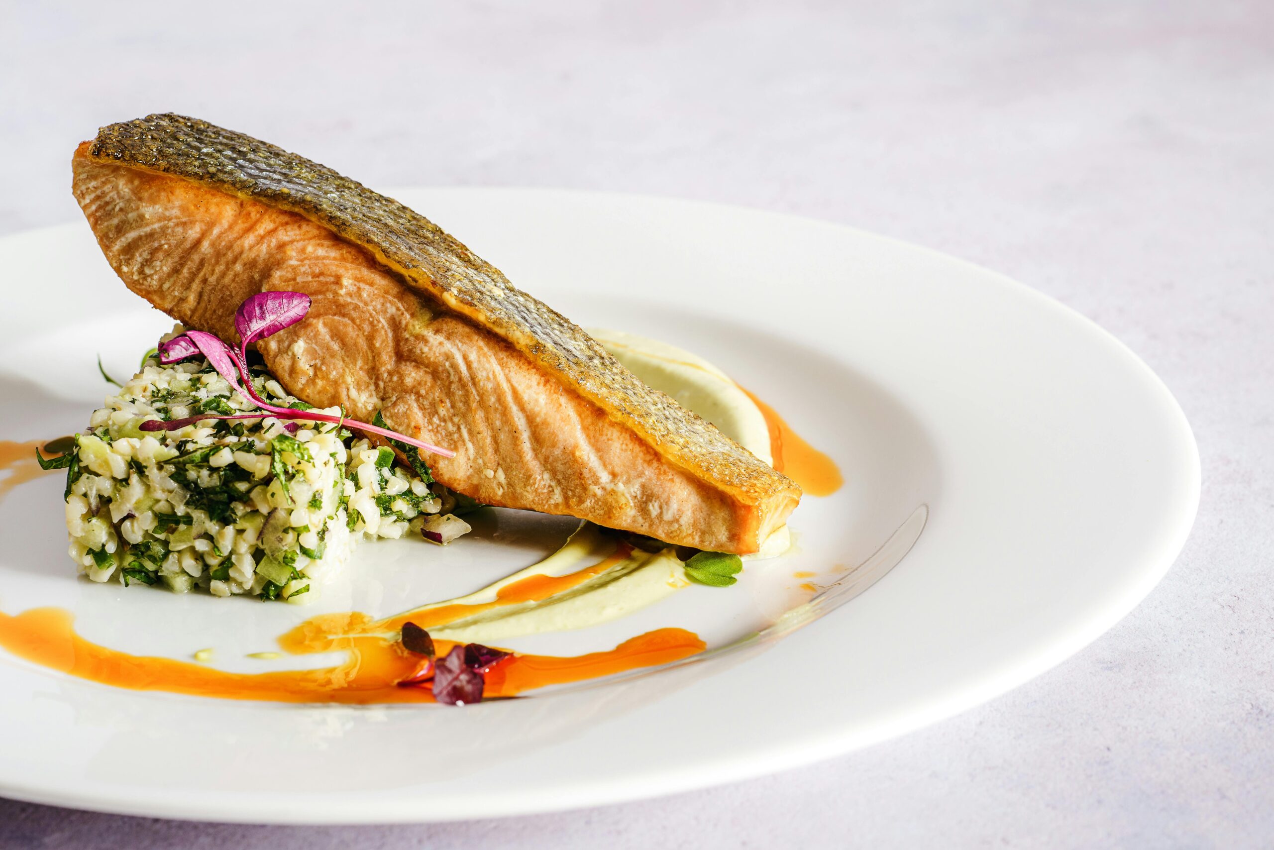 A beautifully plated salmon dish with quinoa, herbs, and a vibrant sauce, perfect for gourmet food lovers.