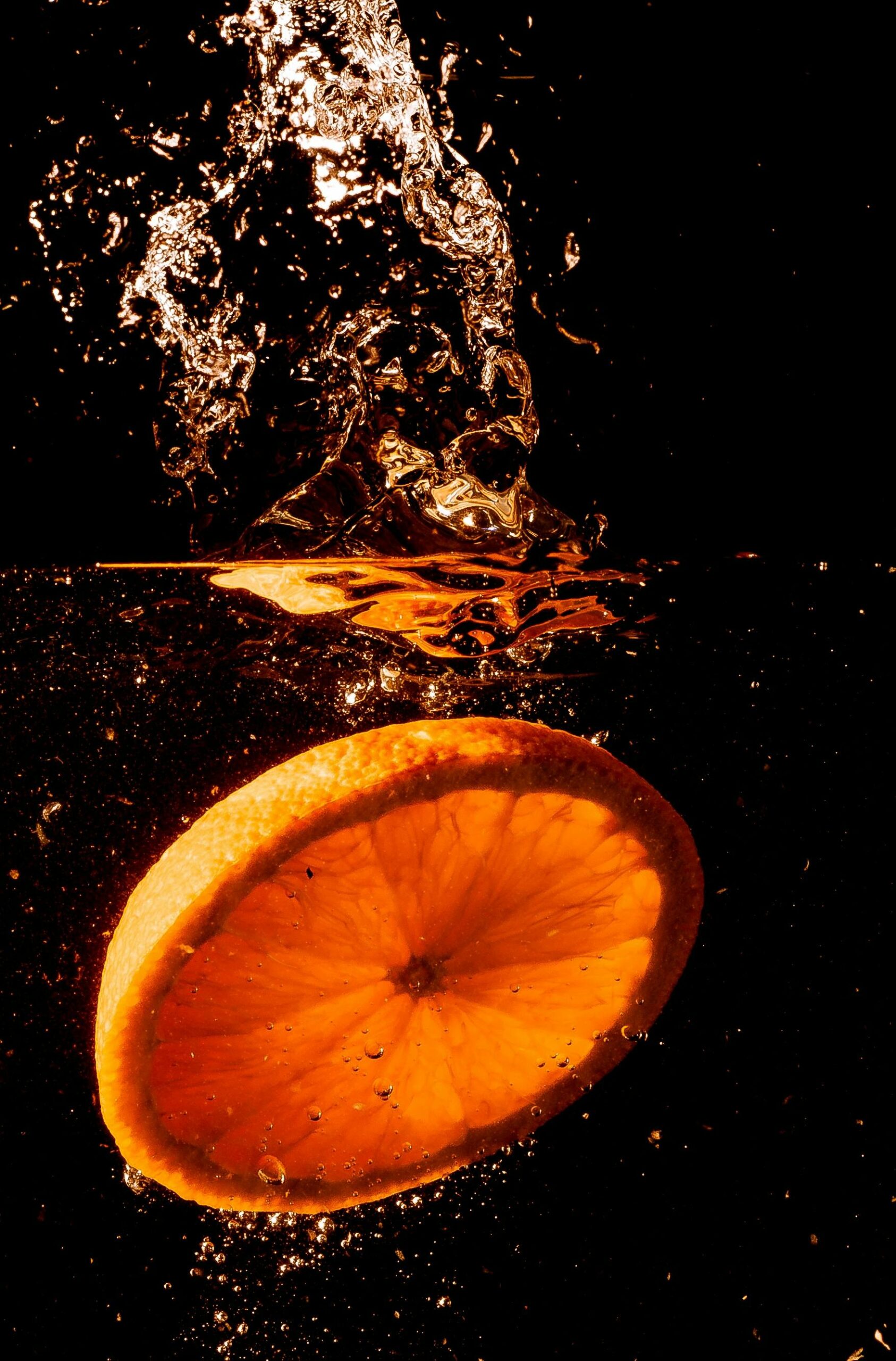 Orange slice creates a splash in water on black background, capturing freshness and energy.