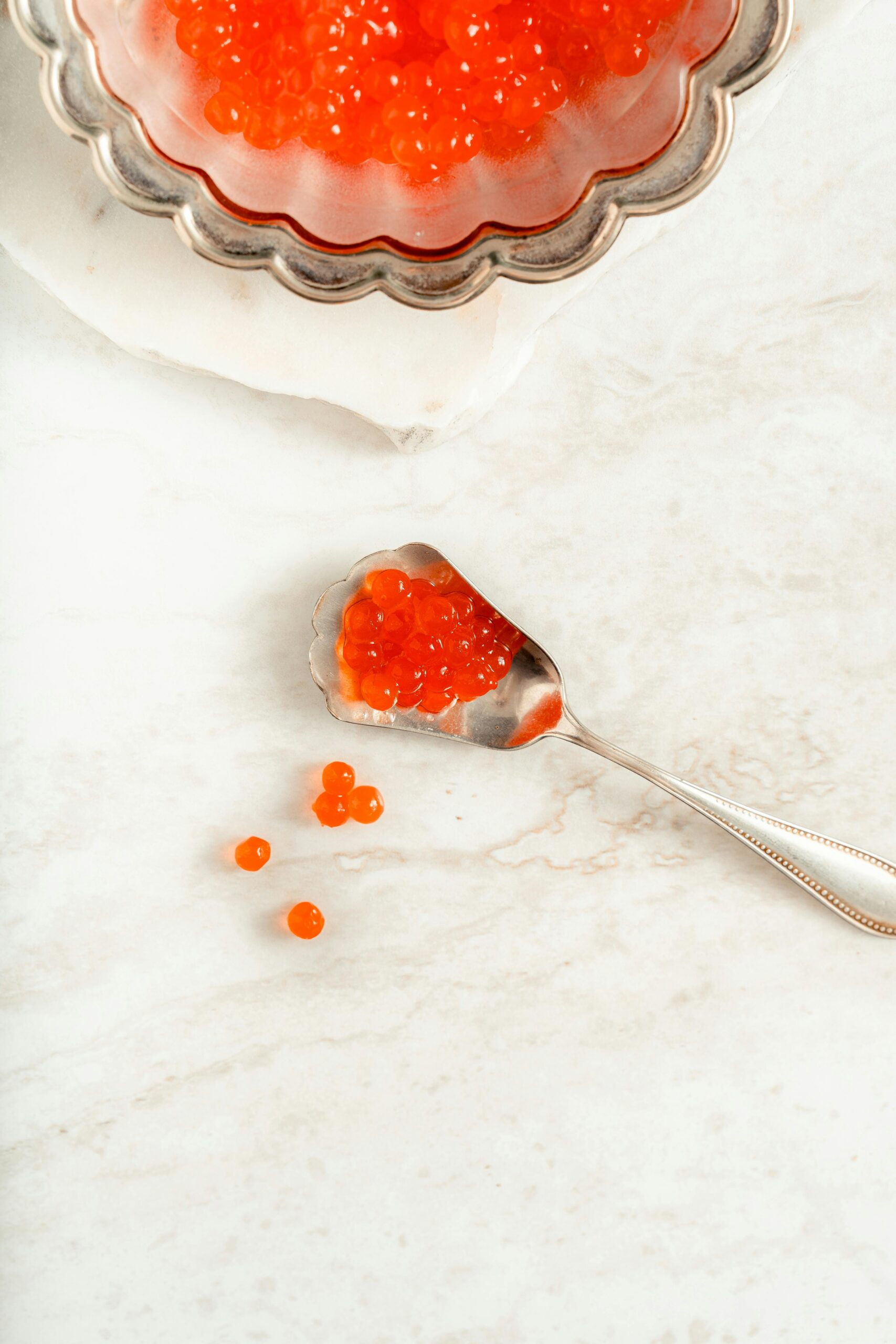 Close-up of luxurious red caviar on a silver spoon over a marble surface.